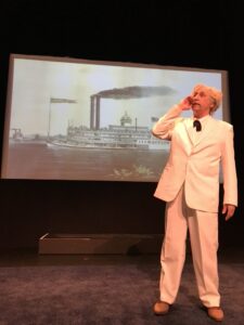 Mark Twain actor stands in front of a steamship background